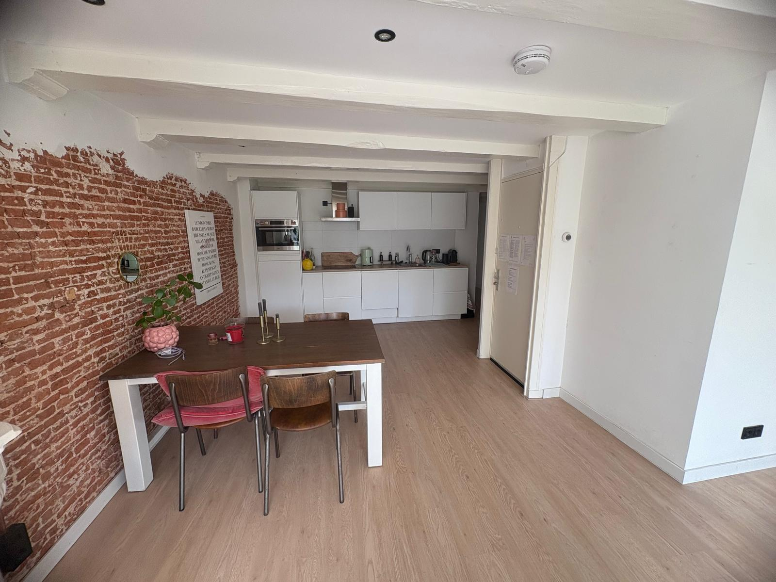 Open-plan living and dining area with exposed brick wall and modern kitchen