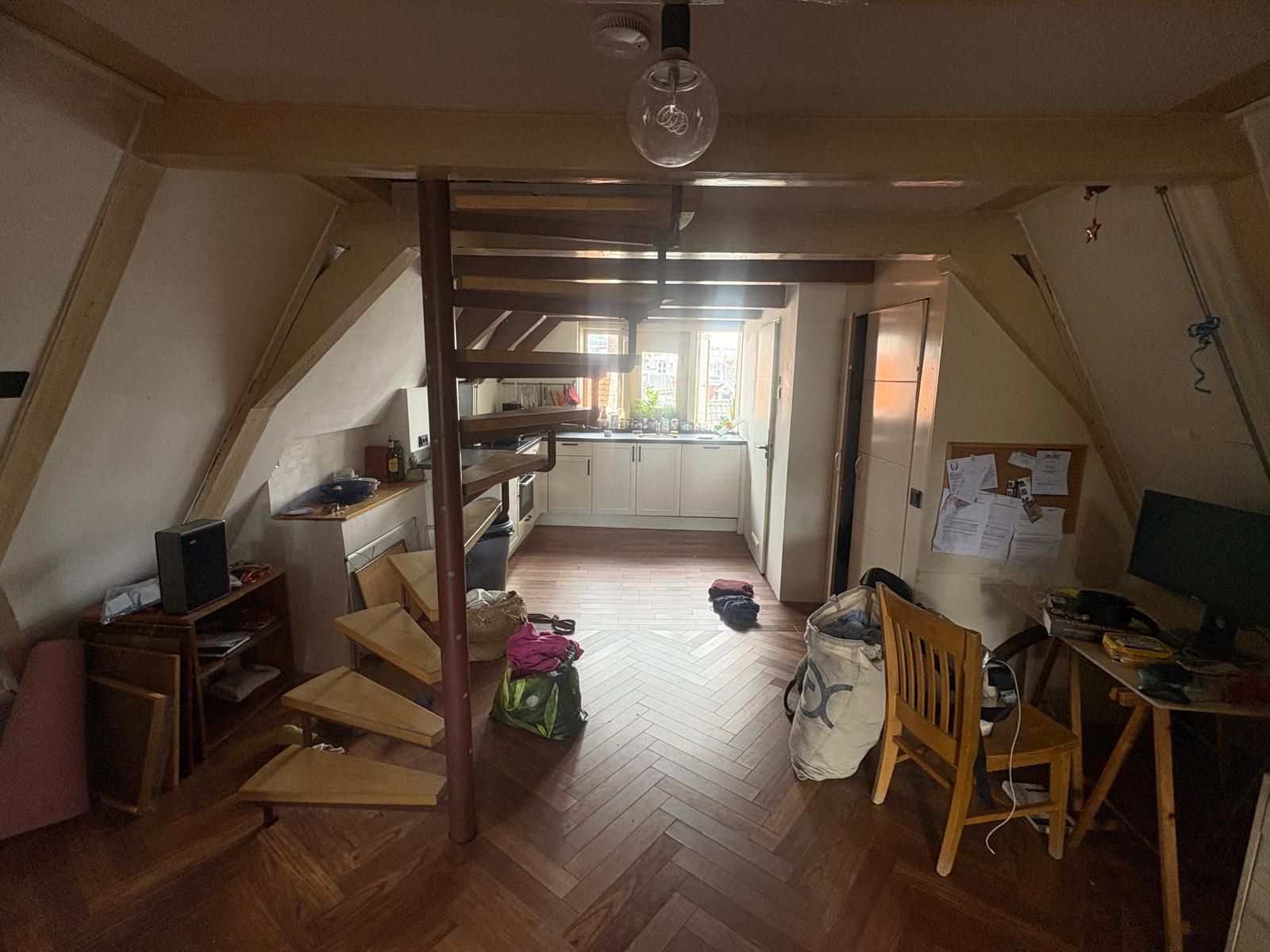 Open-plan living area with exposed burgundy beam, herringbone flooring, and kitchen